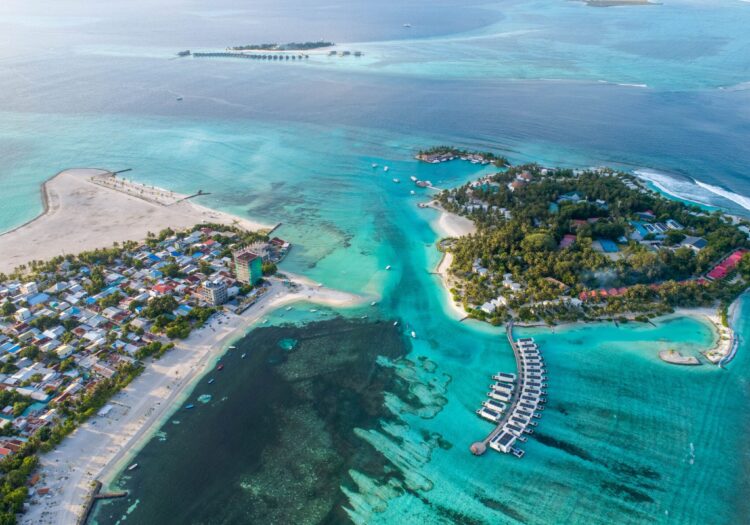 Aerial view of a tropical island with clear turquoise waters and overwater bungalows in the Maldives An aerial view of a tropical island with clear turquoise waters and overwater bungalows in the Maldives